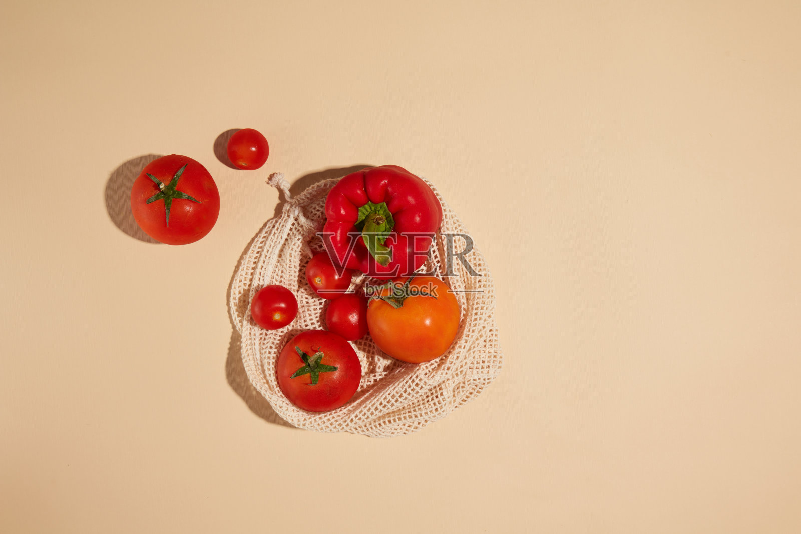 创意照片高角度拍摄的红色蔬菜组成，红色的甜椒和成熟的番茄在白色网袋，放在黄色的台面。设计及广告位照片摄影图片