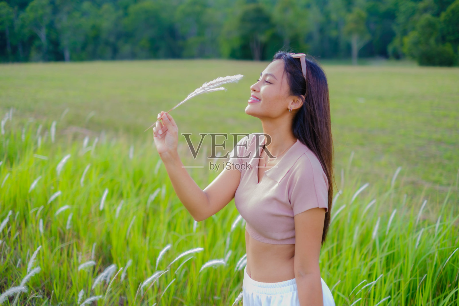 一个年轻的亚洲女人走在草地中间。照片摄影图片