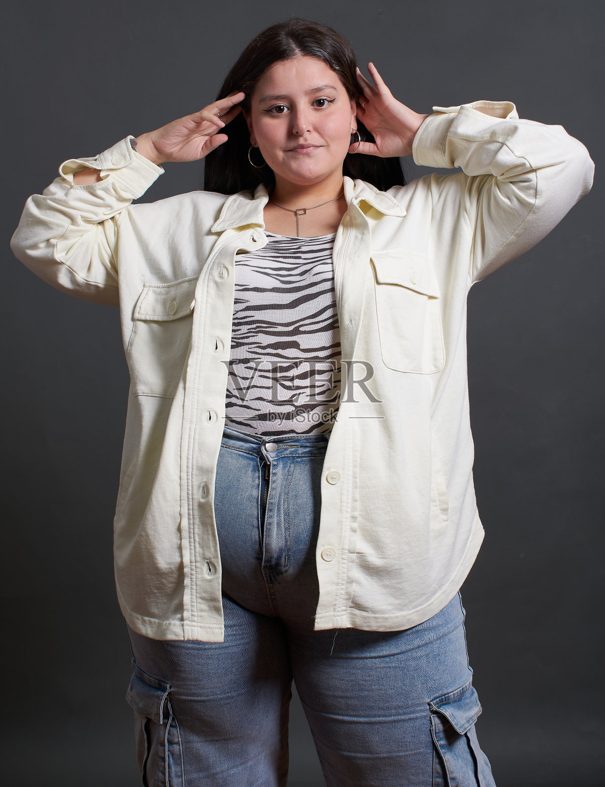 十几岁的拉丁女孩穿着白衬衫和蓝色牛仔裤摆姿势拍照。她穿着斑马印花衬衫，双手抱在头上。画面有一种随意、轻松的气氛。照片摄影图片