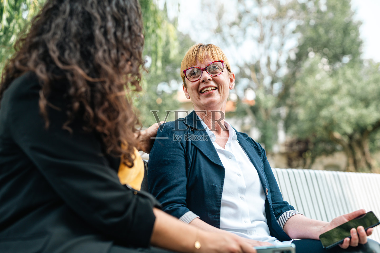 两个同事在他们的空闲时间在公园里放松，分享想法和故事。显示电话照片摄影图片
