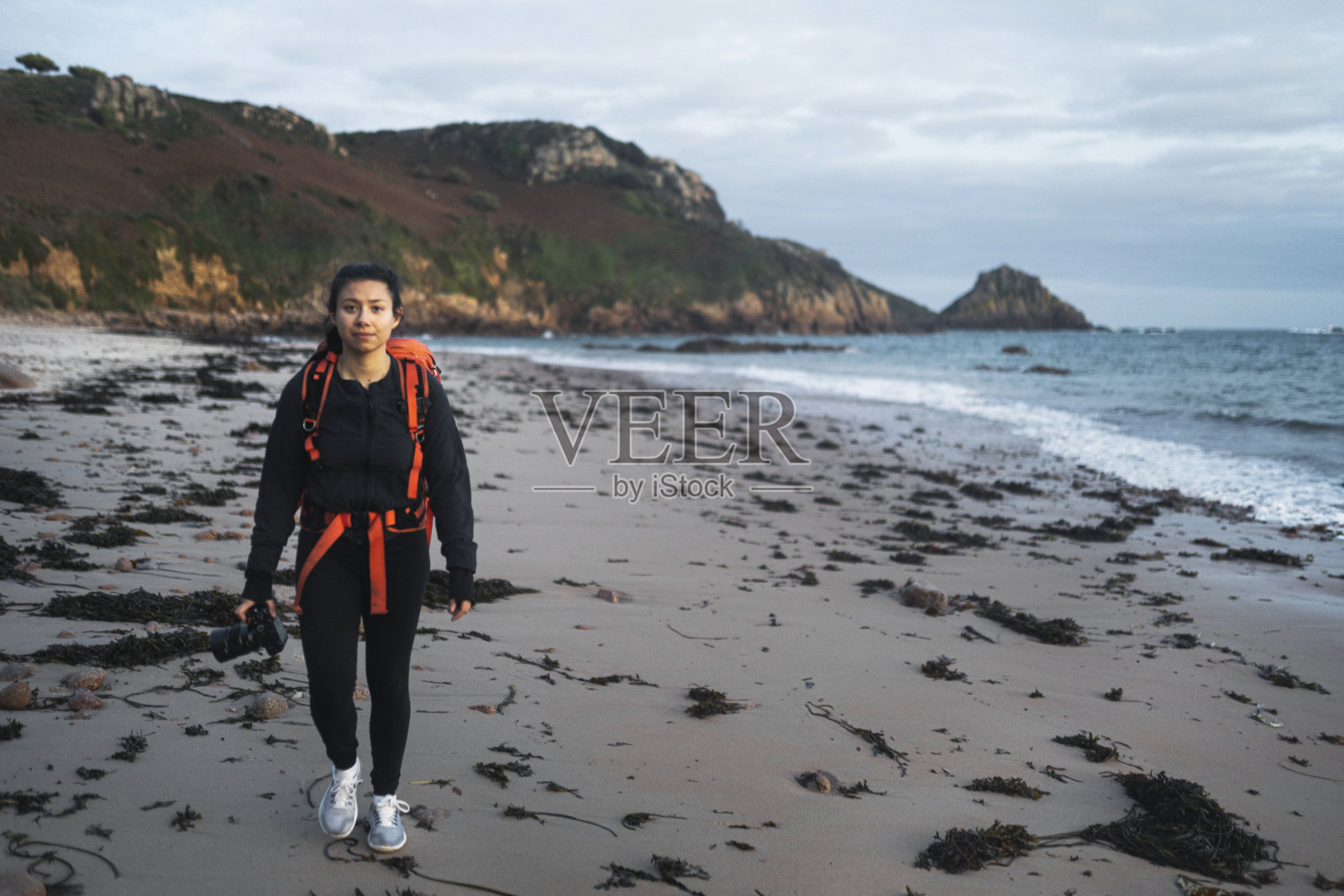 女摄影师沿着海峡群岛波特莱特湾的海滩散步照片摄影图片