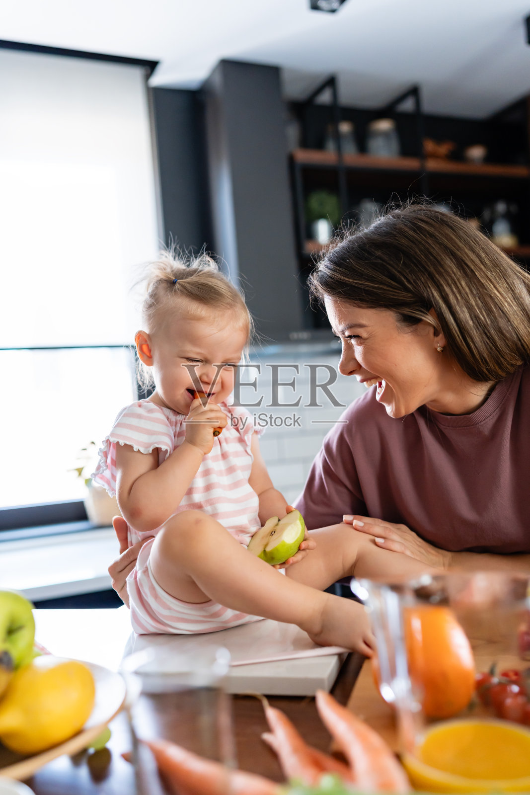 快乐的妈妈和她可爱的小宝宝正在厨房里吃健康的水果和蔬菜照片摄影图片