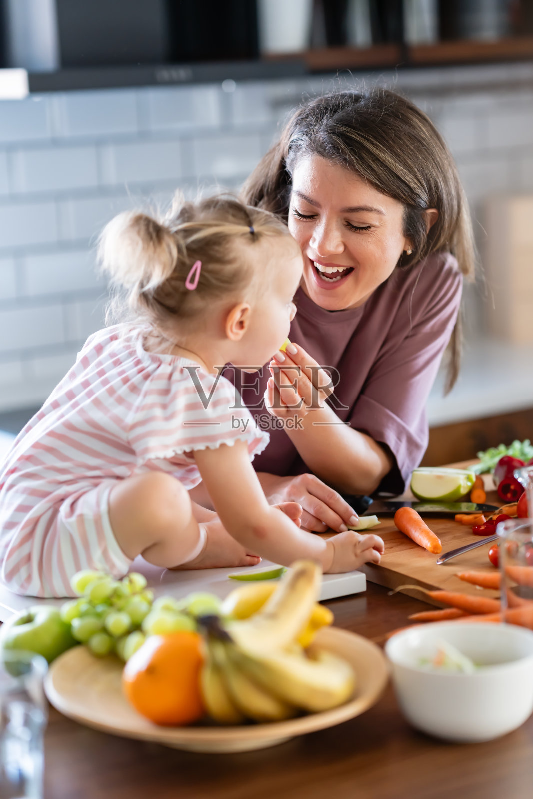 这位母亲准备了一顿富含维生素的健康水果和酸奶餐，她正在家里的厨房柜台上喂她可爱的小女儿照片摄影图片