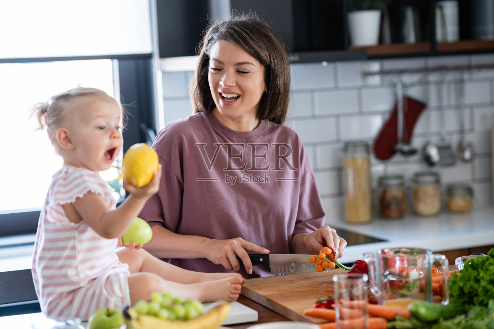 快乐的妈妈正在做一顿有很多水果和蔬菜的健康餐，她可爱的小女儿在陪着她照片摄影图片