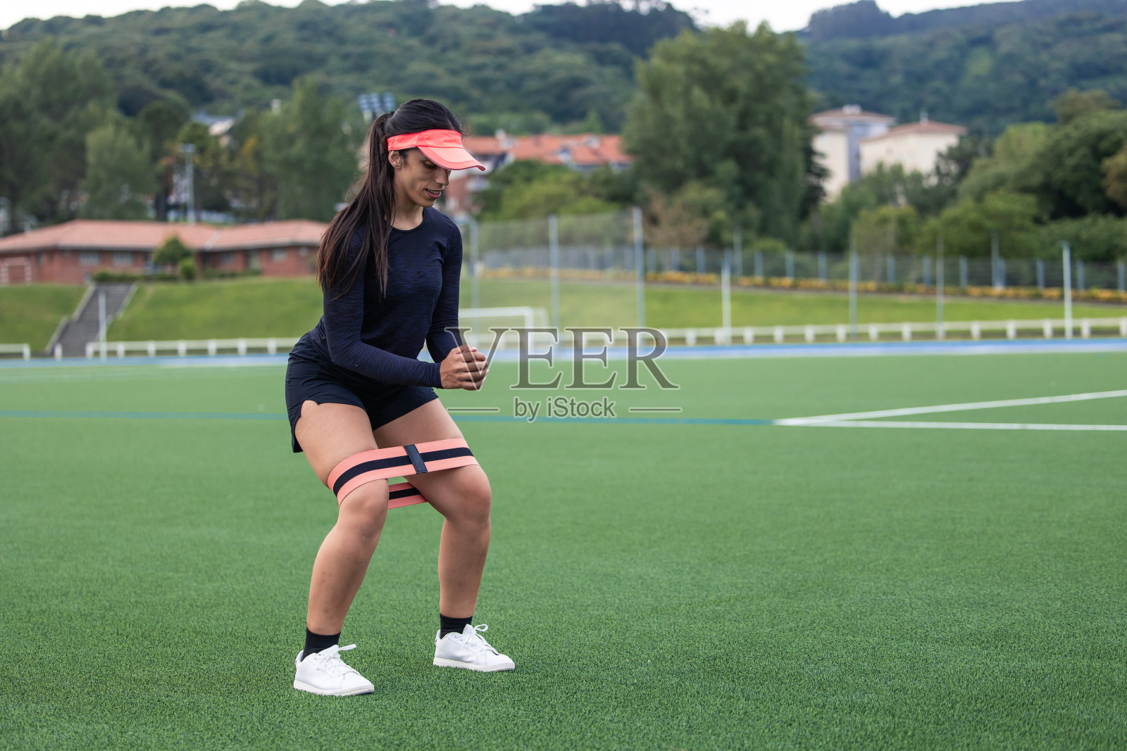 女运动员戴帽训练腿在足球场上与阻力带照片摄影图片