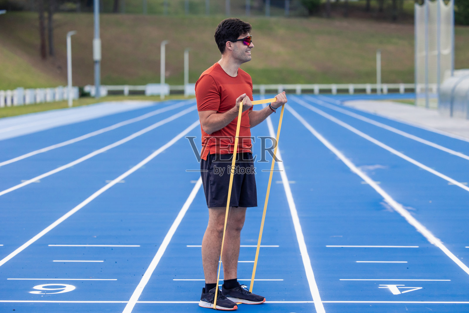 戴太阳镜的运动员在户外跑道上用阻力带加强肱二头肌照片摄影图片