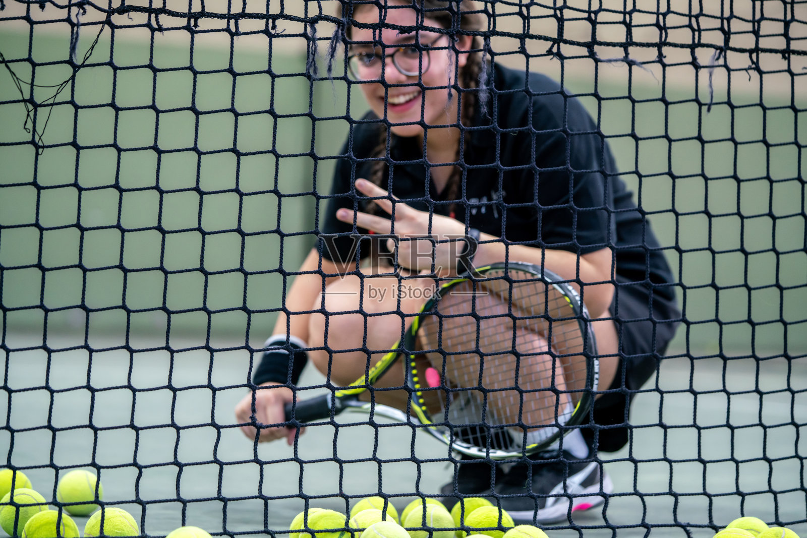 十几岁的女网球运动员在网上，网上是前景，重点是前景，女网球运动员是背景，在硬地水平仍然照片摄影图片