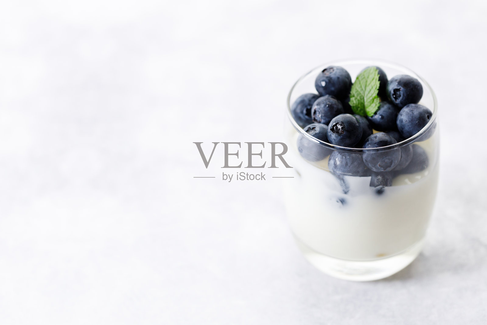 成熟的有机蓝莓和酸奶在白色的石头桌子背景玻璃。有选择性的重点。照片摄影图片