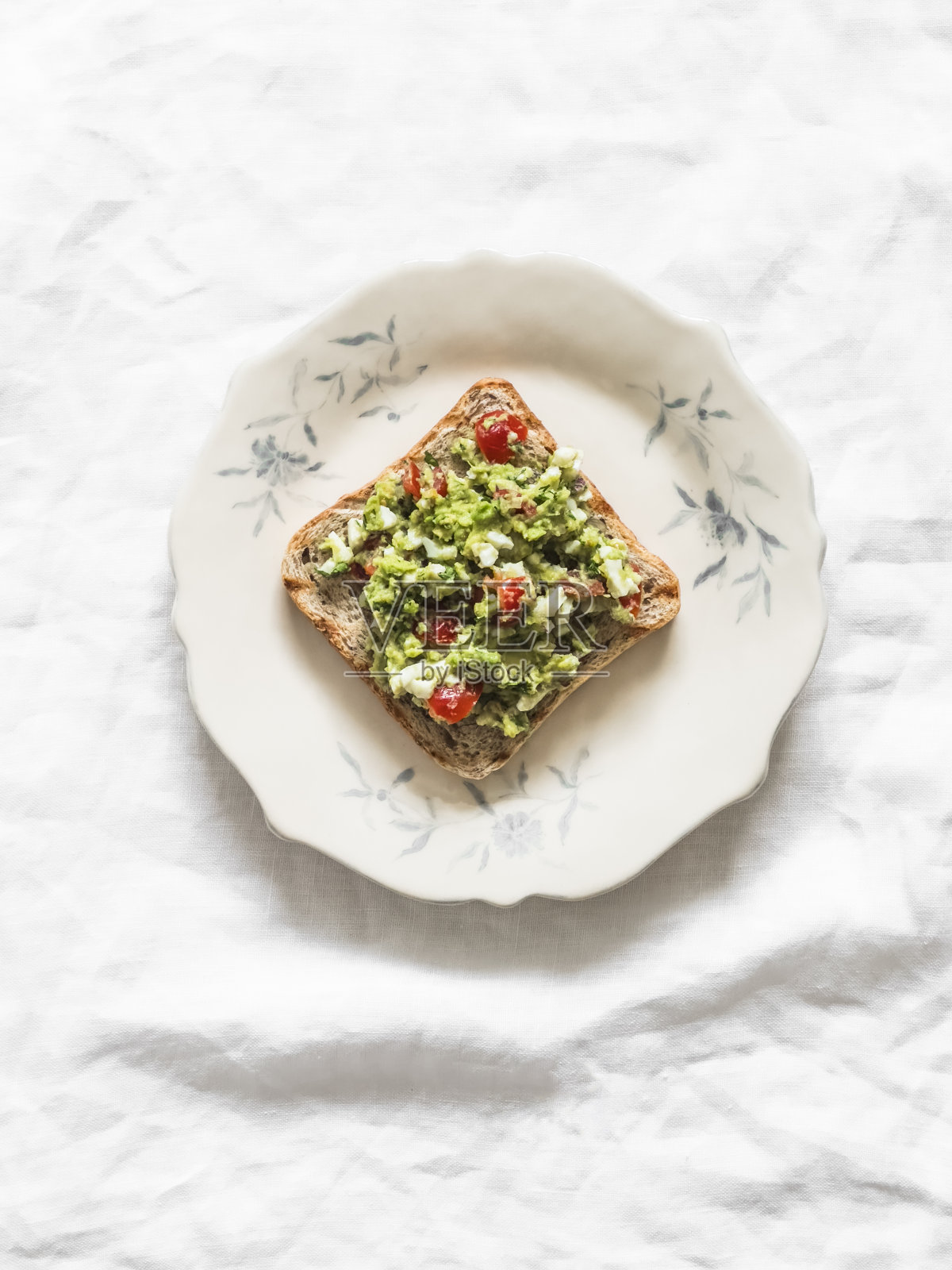 牛油果、鸡蛋、红洋葱、圣女果铺在全谷物烤面包三明治上，浅色背景，俯视图照片摄影图片