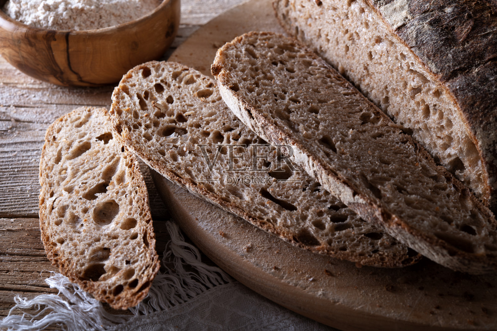 自然发酵的面包，切菜板上的切片全麦面包，旧木桌上的一碗面粉，特写。照片摄影图片