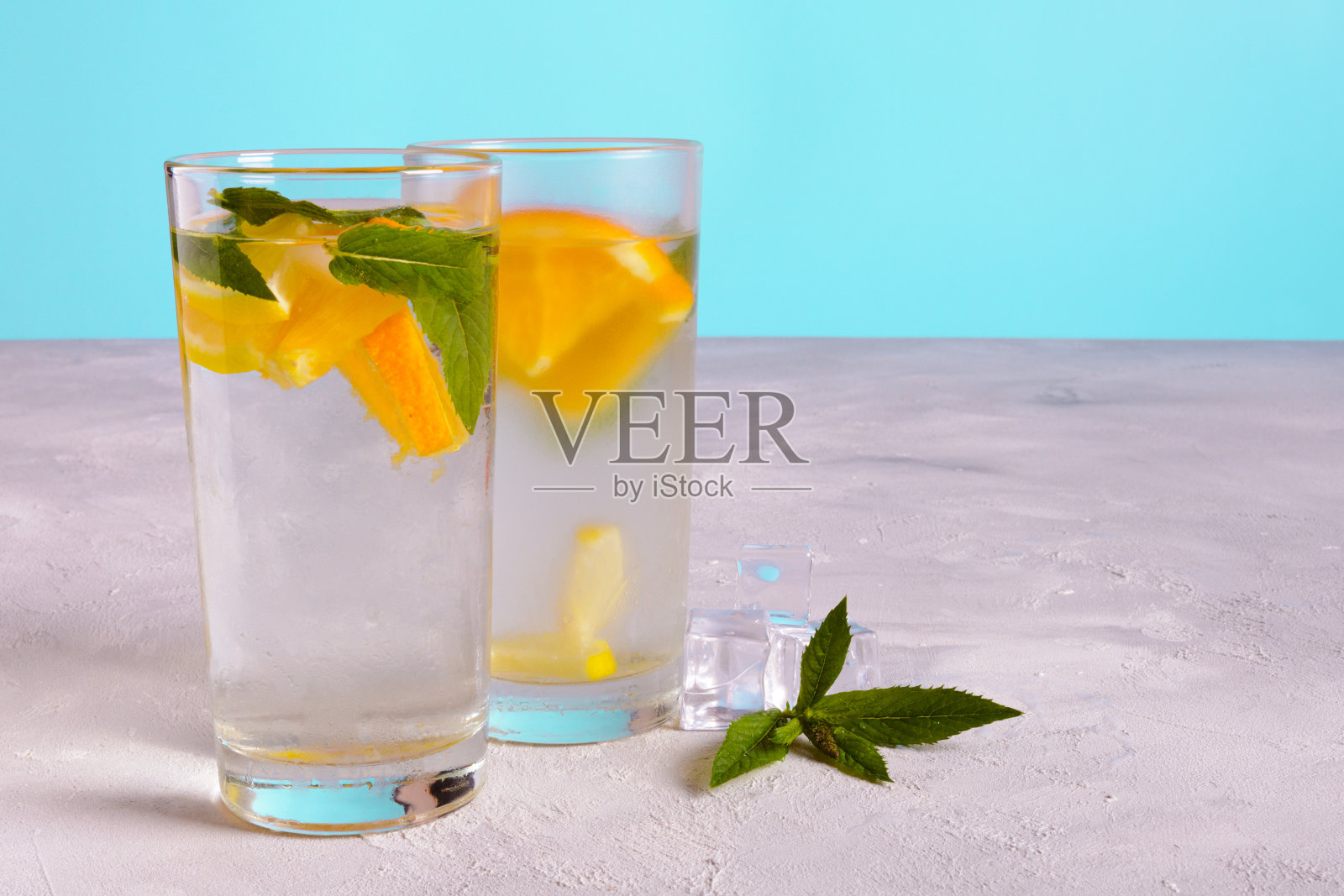 两杯水，橙片和新鲜薄荷叶放在灰色的表面上，蓝色的背景照片摄影图片