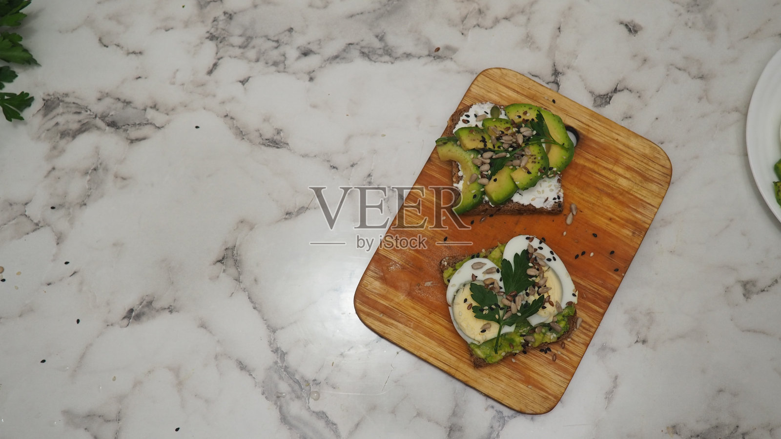 健康的牛油果吐司配黑麦面包、牛油果切片、鸡蛋、白干酪、南瓜子、坚果和芝麻，早餐或午餐。素食。素食菜单。食物配方，健康饮食，生酮饮食照片摄影图片