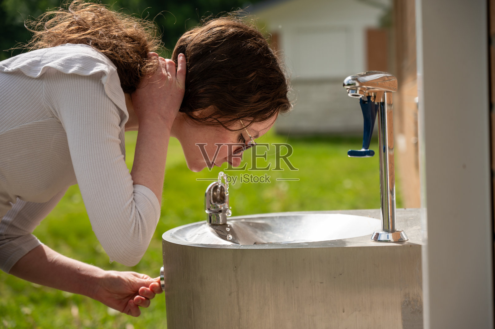 年轻女子在饮水机旁喝酒照片摄影图片