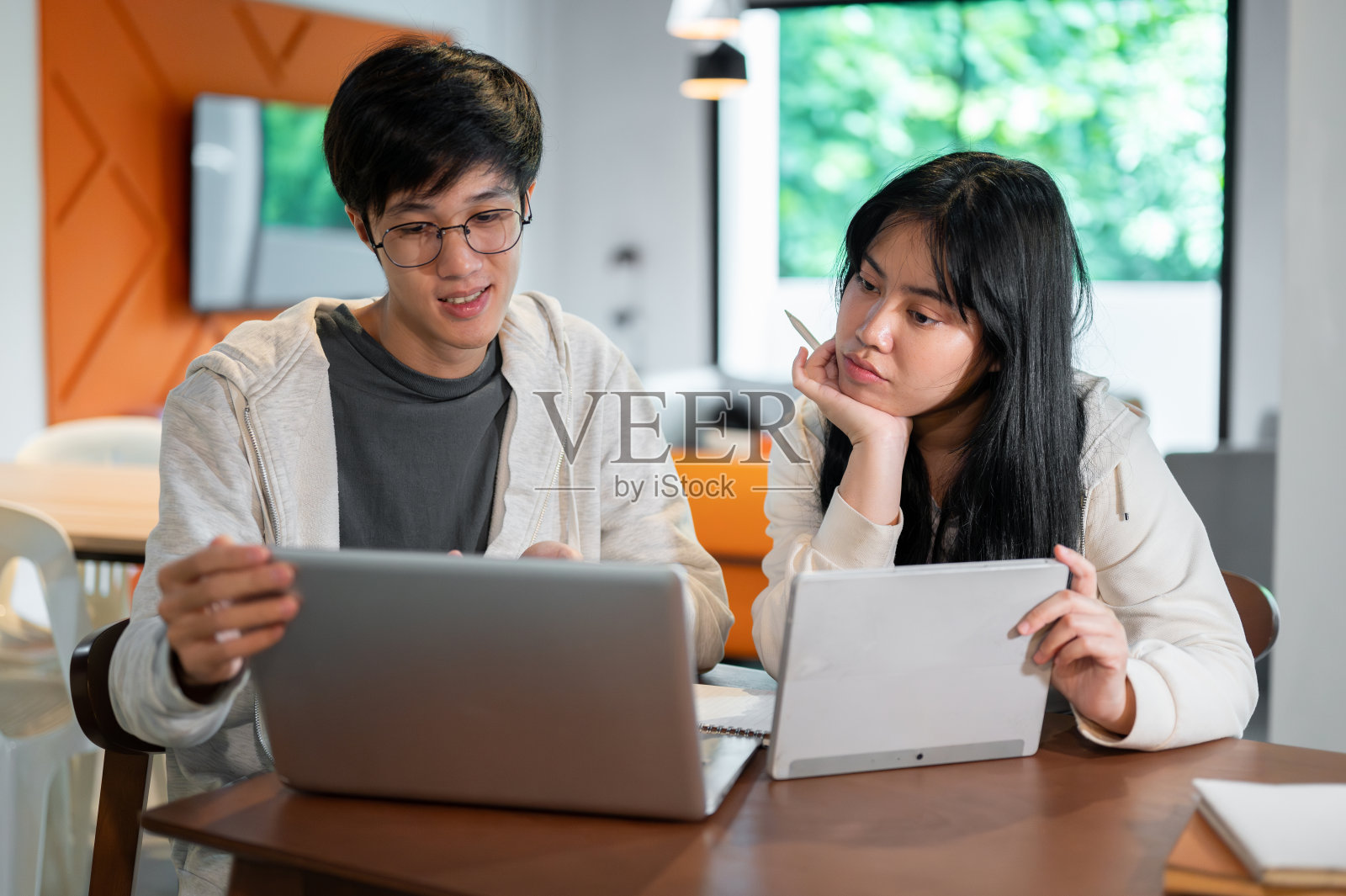 两个年轻的亚洲大学生正在咖啡馆或图书馆讨论一个合作项目。照片摄影图片