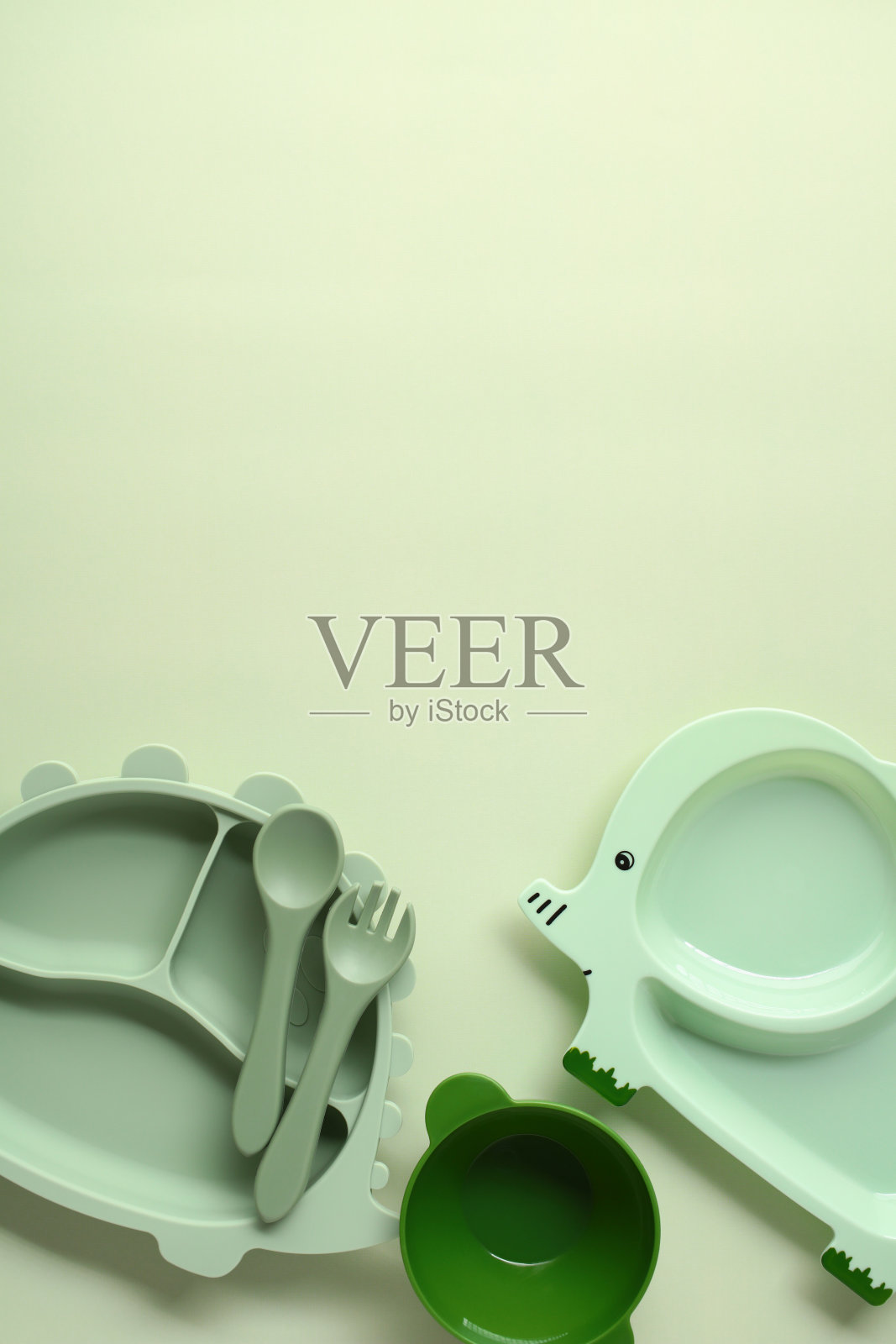 可爱的大象形状和恐龙形状的婴儿盘子，餐具和一个小碗在柔软的绿色背景上照片摄影图片