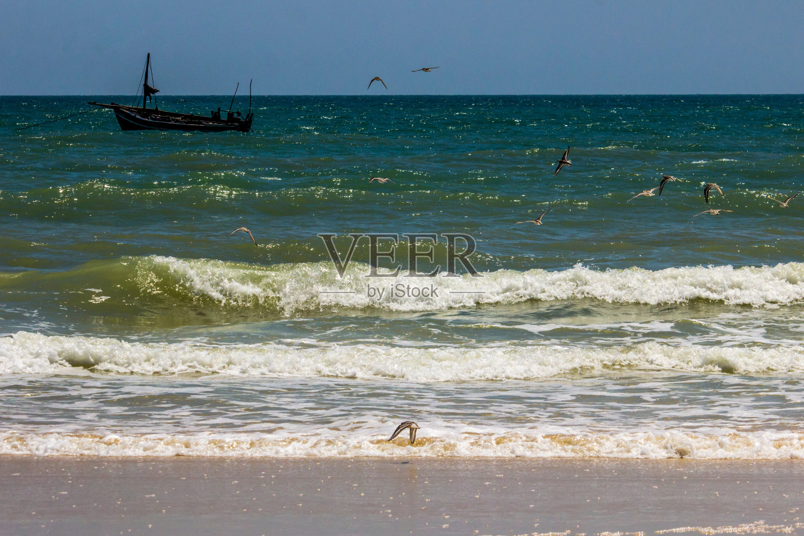 一群涉水者在莫桑比克因哈索罗海滩上飞行，背景是一艘小渔船。照片摄影图片