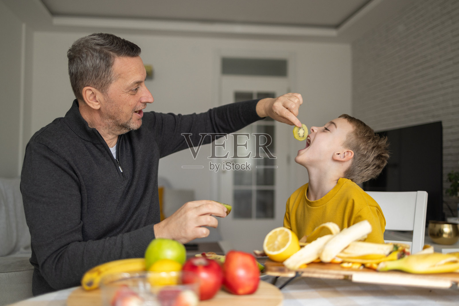 父子俩在客厅里玩水果。照片摄影图片
