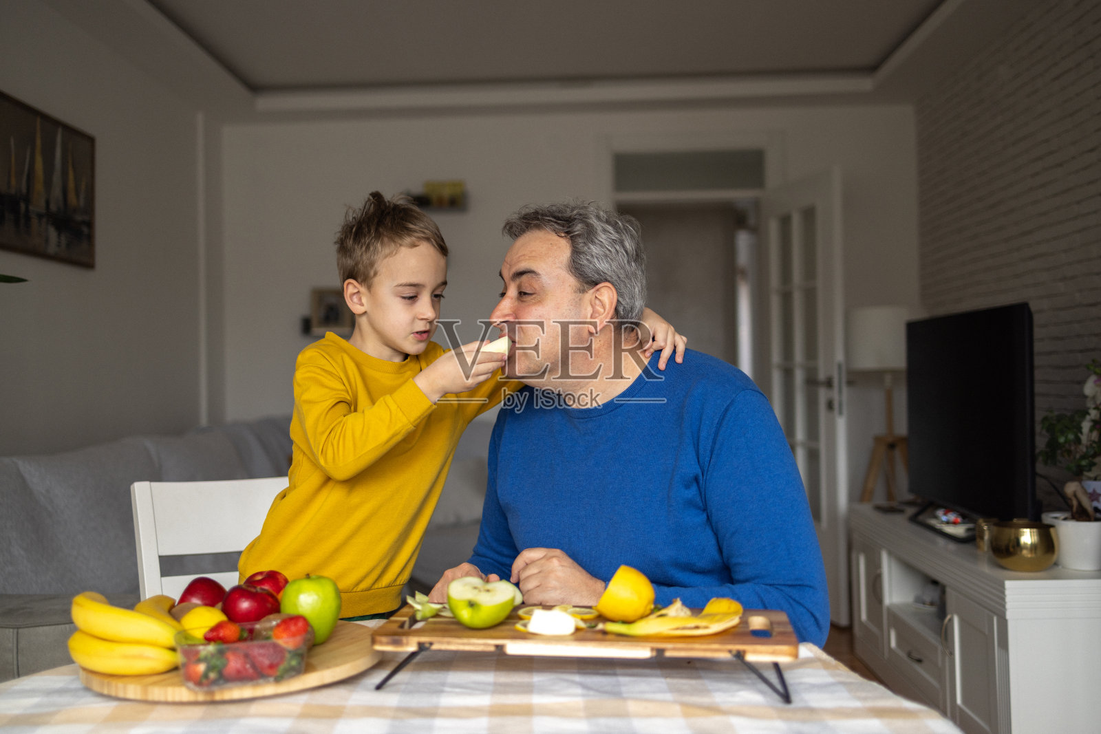 父子俩在客厅吃水果。照片摄影图片