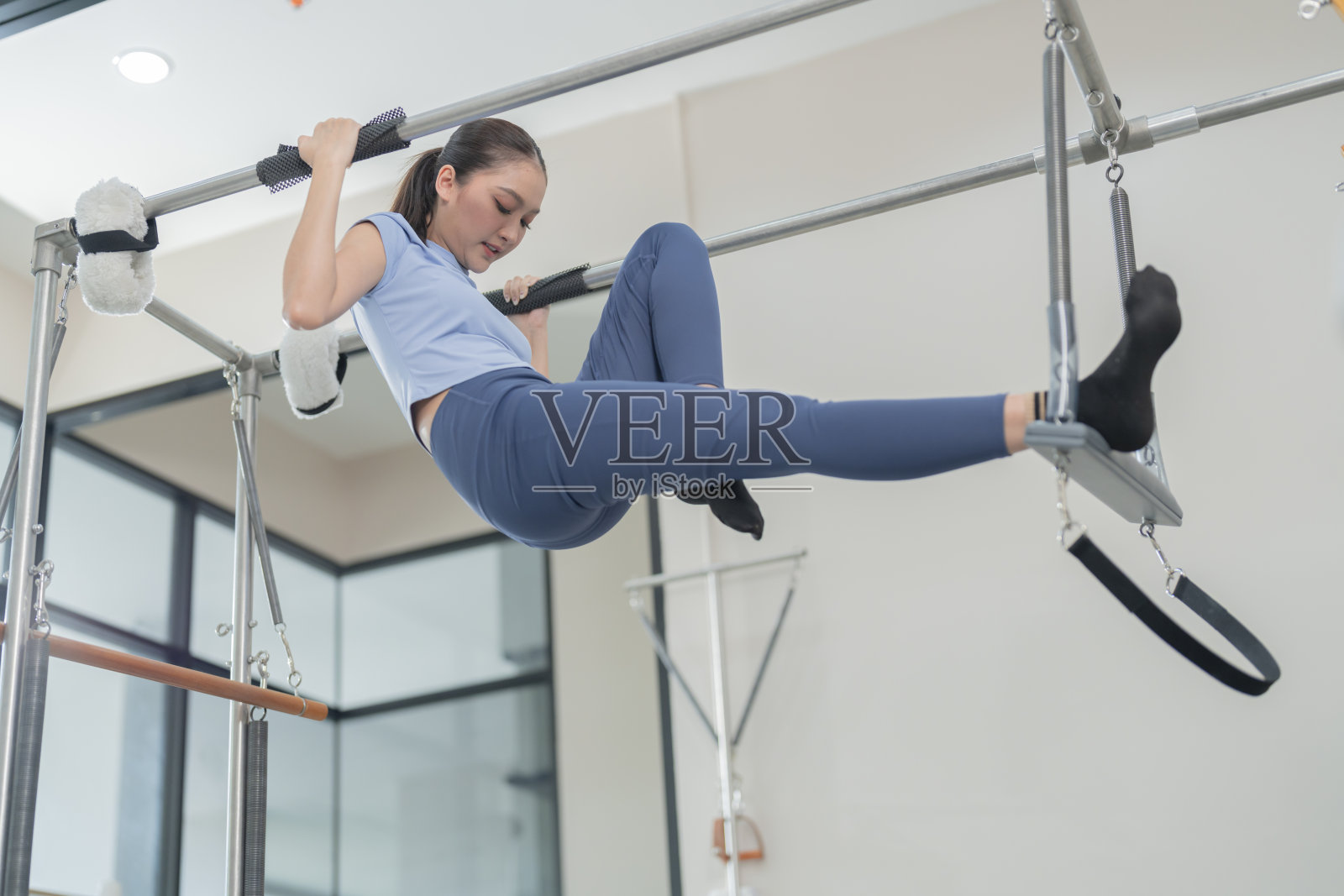 女普拉提教练在健身房普拉提机上锻炼女子在半空中保持身体平衡一名女子在健身房普拉提课上和教练一起做普拉提塑形照片摄影图片