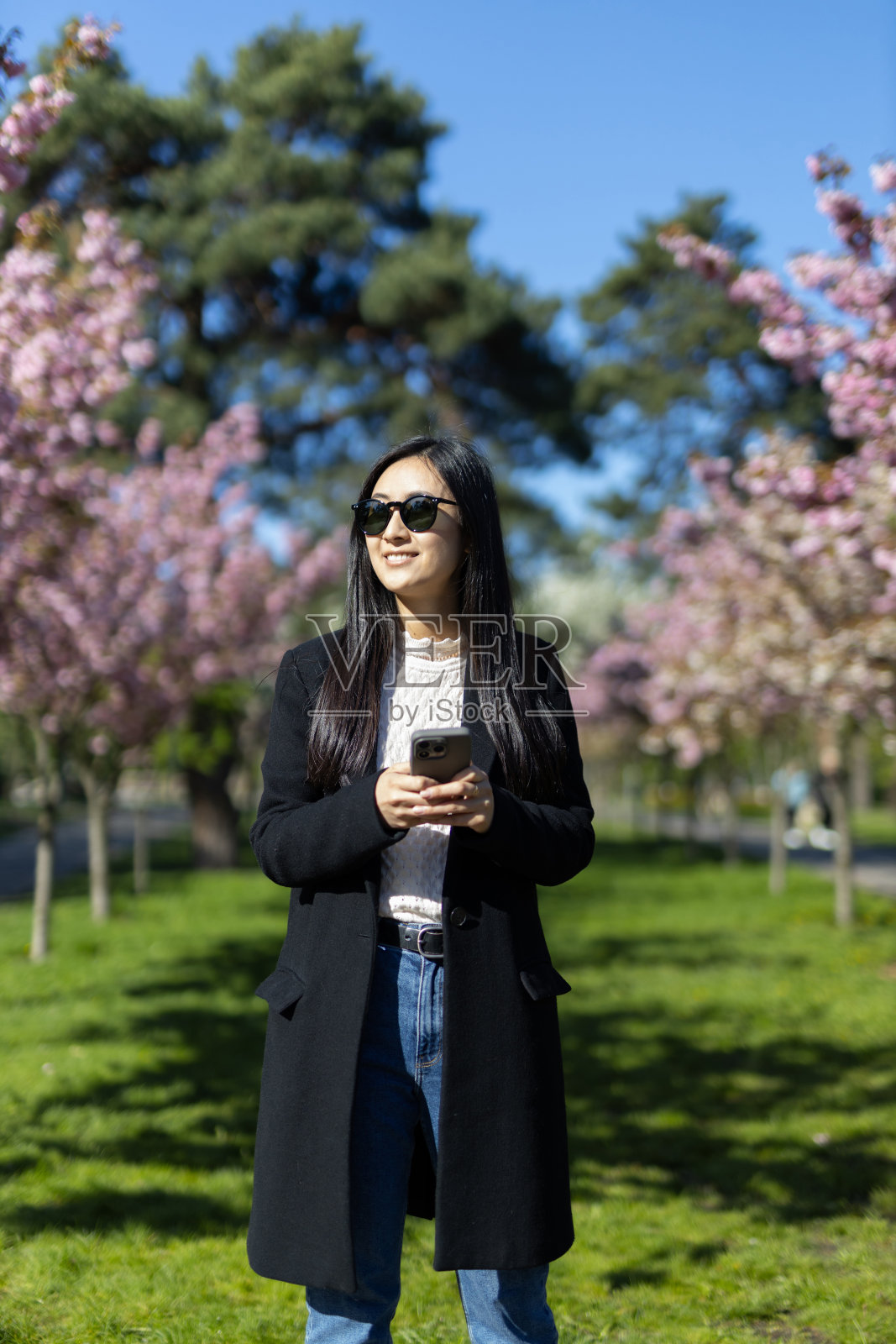 一位快乐的年轻女子戴着墨镜，在樱花盛开的公园里享受春天。照片摄影图片