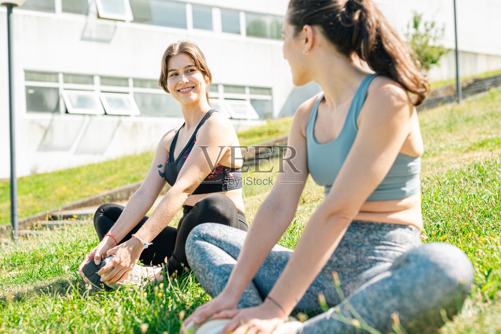 在一个阳光明媚的日子里，两个健康的年轻女子在草地上热身，然后去做她们最喜欢的运动。照片摄影图片