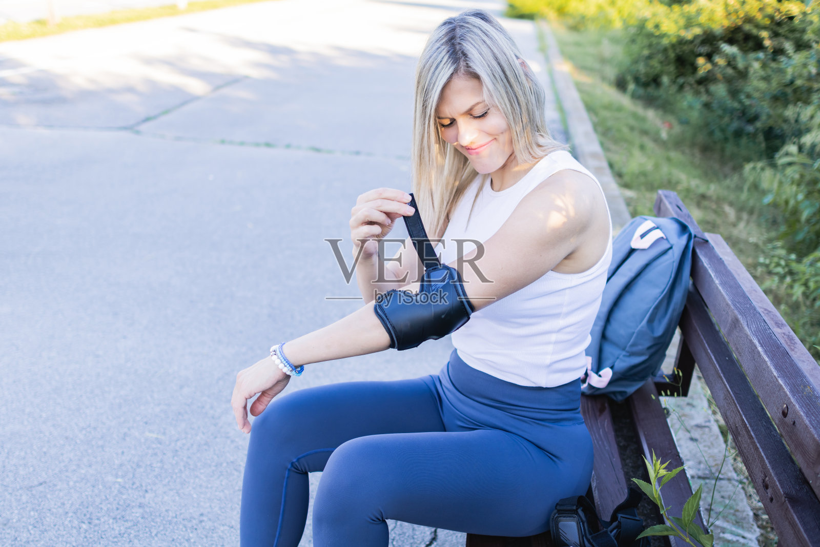 穿着运动服的漂亮女运动员正在为轮滑做准备。她正在系好旱冰鞋，穿上防护装备。照片摄影图片