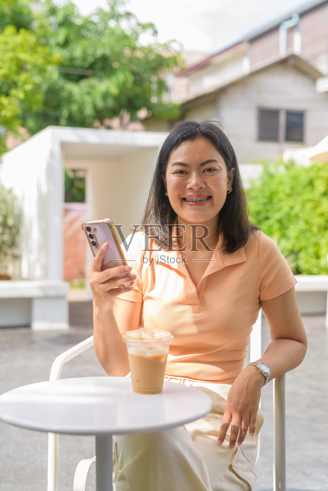 一名女子坐在户外咖啡店里，随意地穿着一件橙色上衣，享受着一杯冰咖啡照片摄影图片