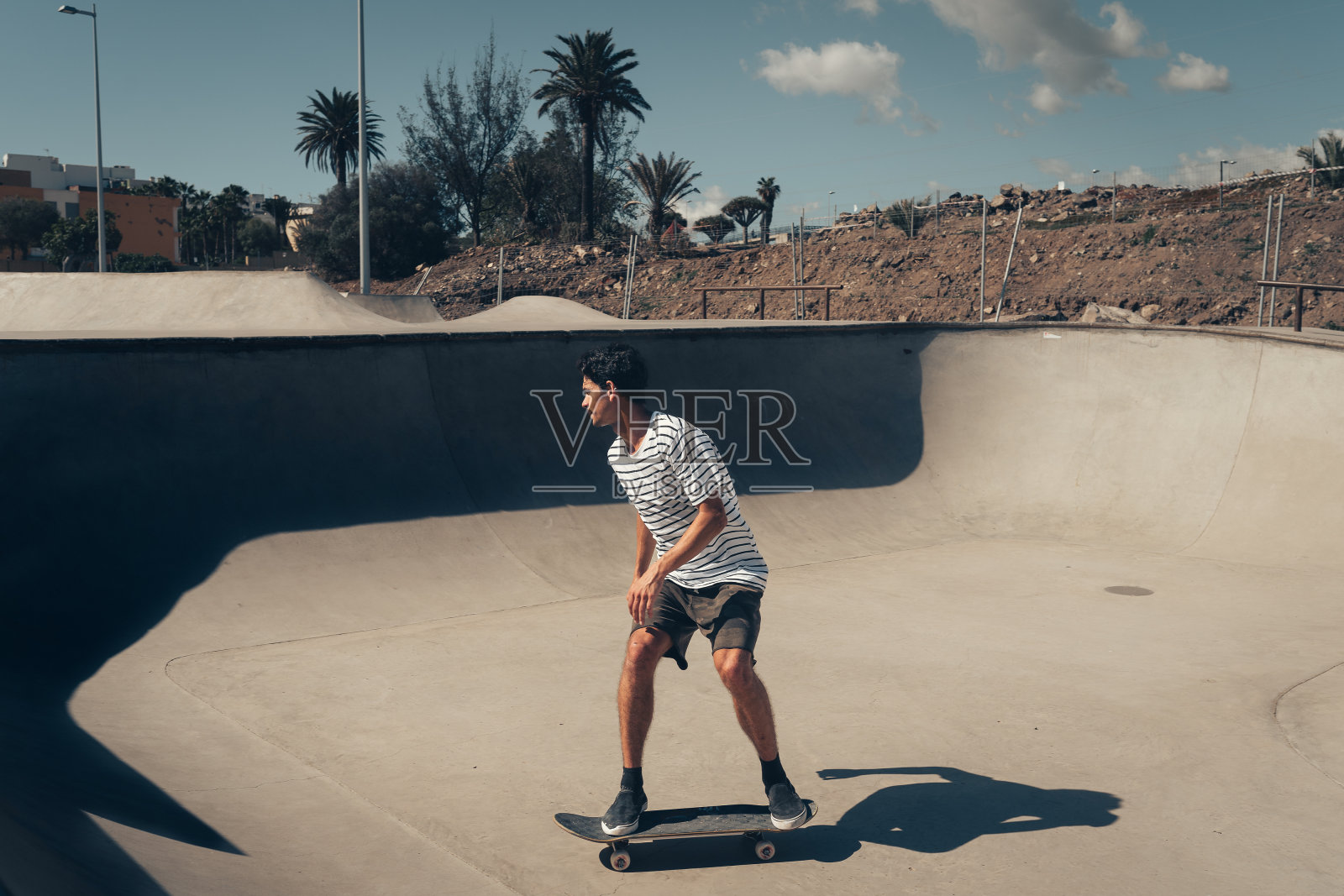 在一个阳光明媚的日子里，一个穿着短裤溜冰鞋的年轻人在溜冰公园里滑冰照片摄影图片