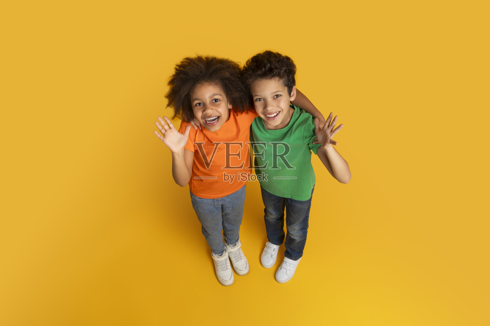 热情的孩子们对着黄色背景的相机挥手照片摄影图片