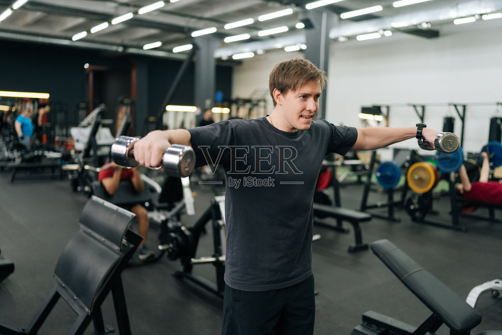 有动力的新手运动员的肖像，很难做侧臂举哑铃练习。疲劳的男运动员用哑铃训练来改善肩膀。照片摄影图片