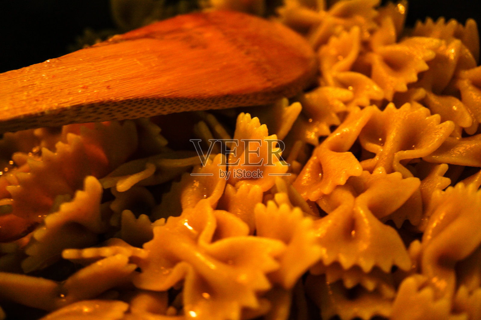 用木勺煮意大利面——用木勺把全谷物倒入锅中照片摄影图片