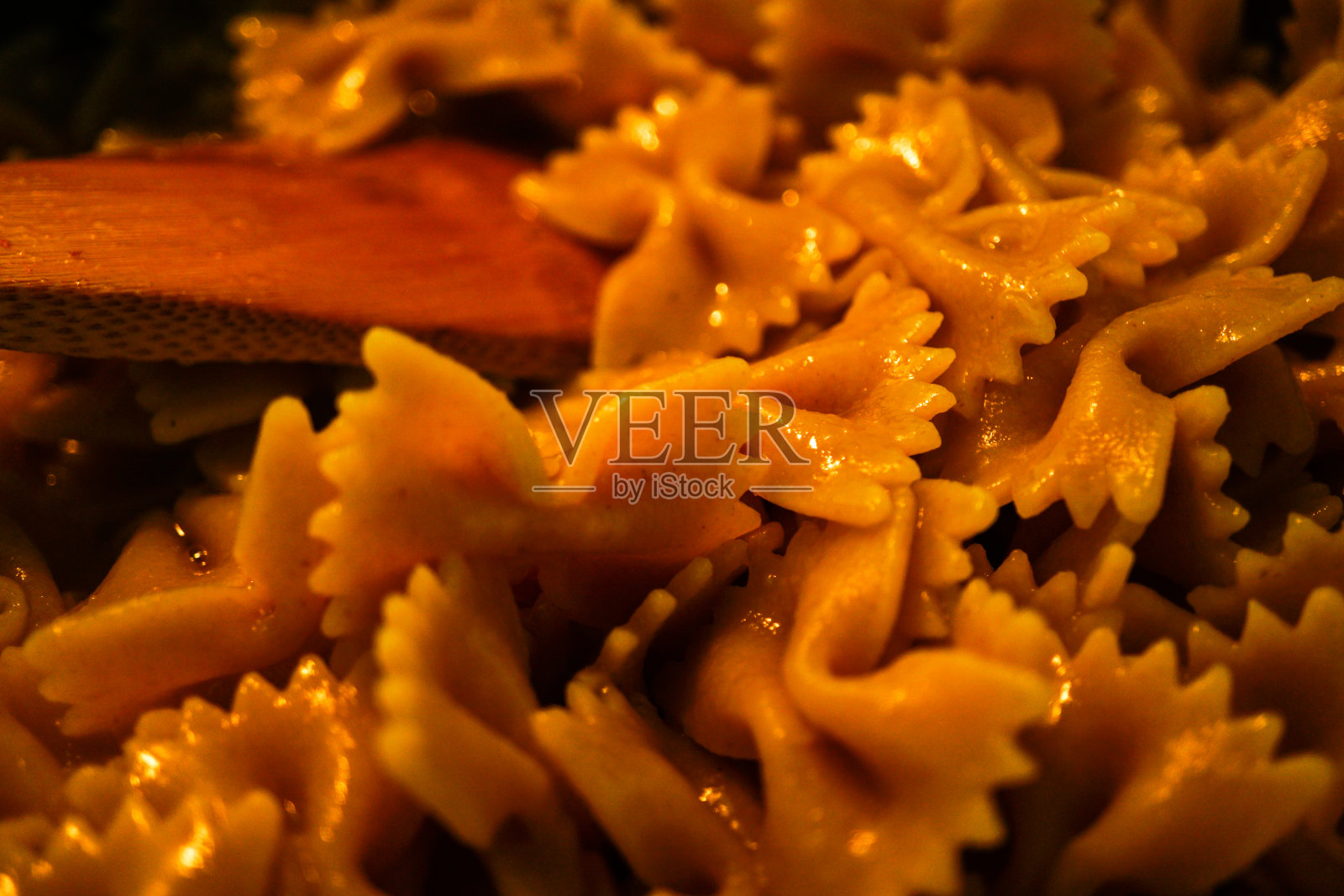 用木勺煮意大利面——用木勺把全谷物倒入锅中照片摄影图片