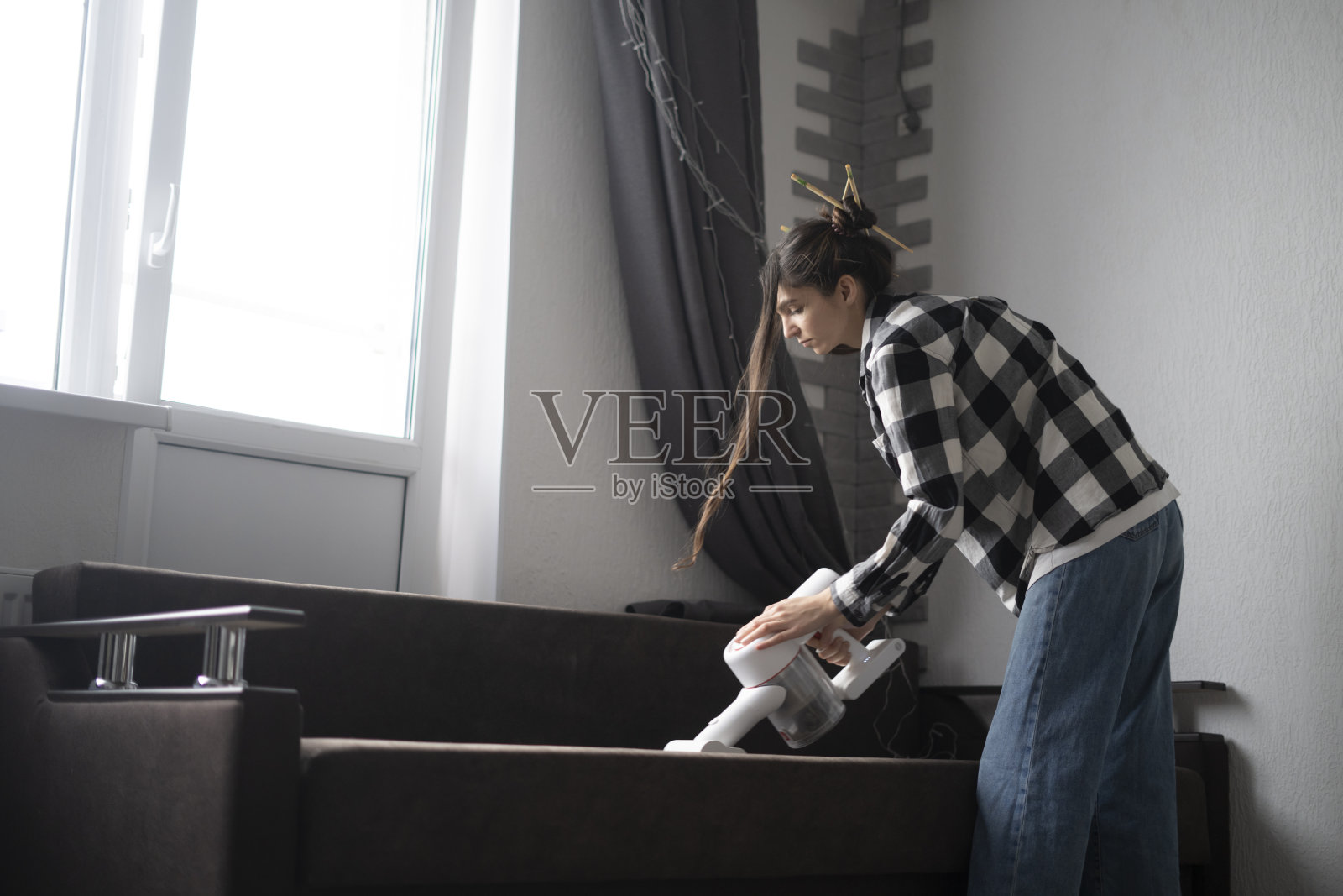 年轻女子在家里明亮房间的沙发上使用手持式吸尘器照片摄影图片