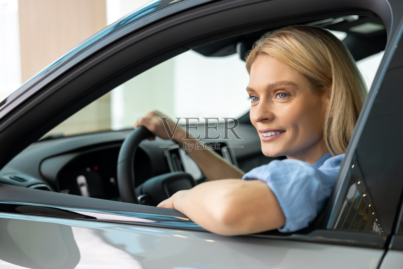 一个穿着蓝衬衫的金发女人坐在一辆车里，看上去很满足照片摄影图片