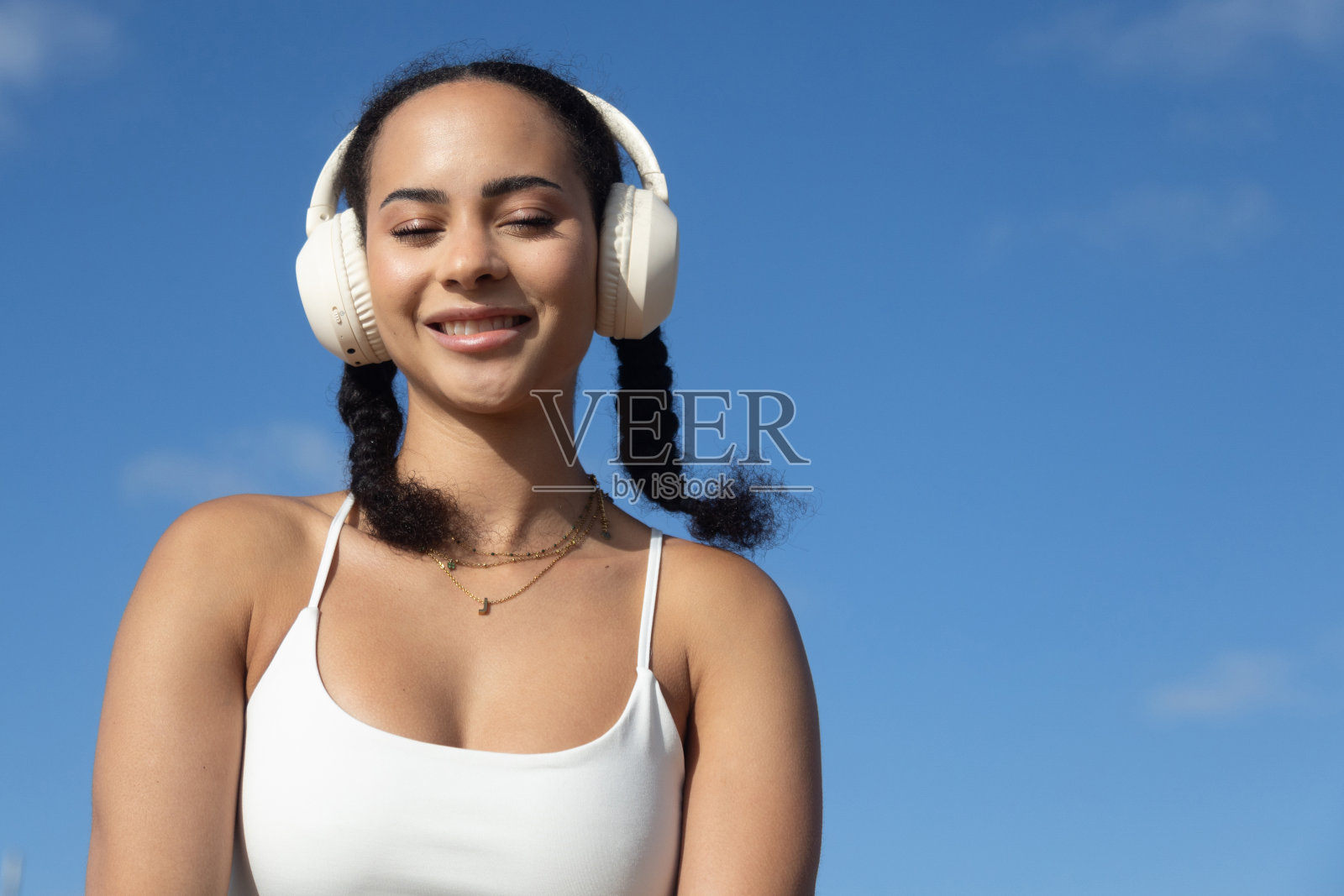 年轻的拉丁女性微笑着闭着眼睛，穿着蓝色天空背景的运动服照片摄影图片