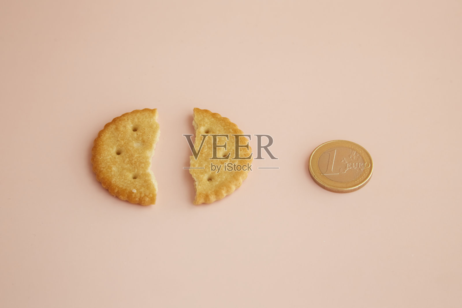一块饼干在粉红色的背景上被掰成两半，旁边是一枚1欧元的硬币，特写，食品价格上涨，为食物买单，为服务付小费照片摄影图片