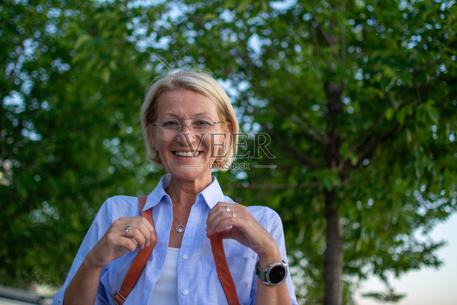一个戴着眼镜的开朗成熟的金发女人在城市公园里愉快地散步的画像照片摄影图片