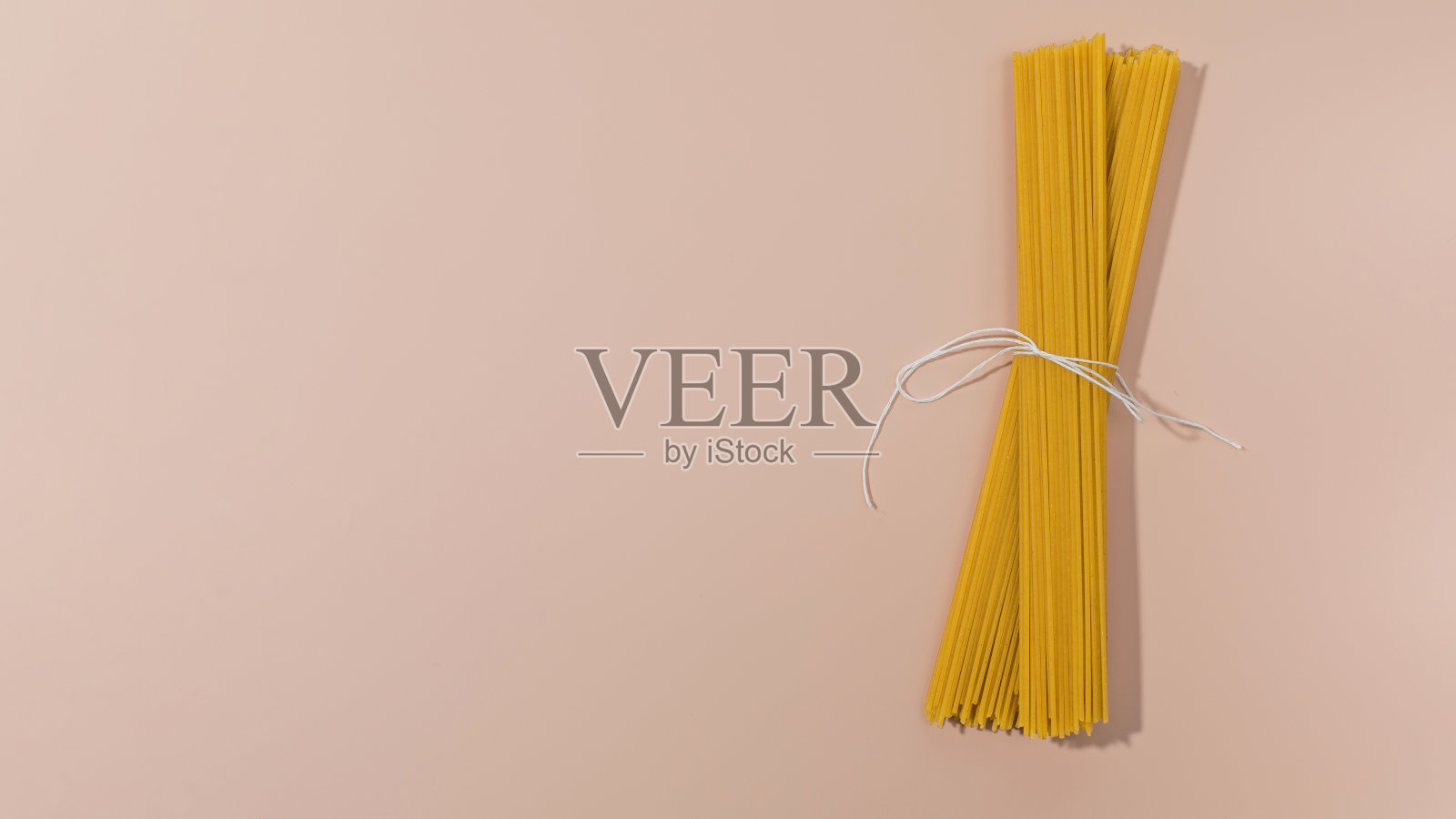 粉红色背景上用绳子绑着的一束生意大利面条。本空间照片摄影图片