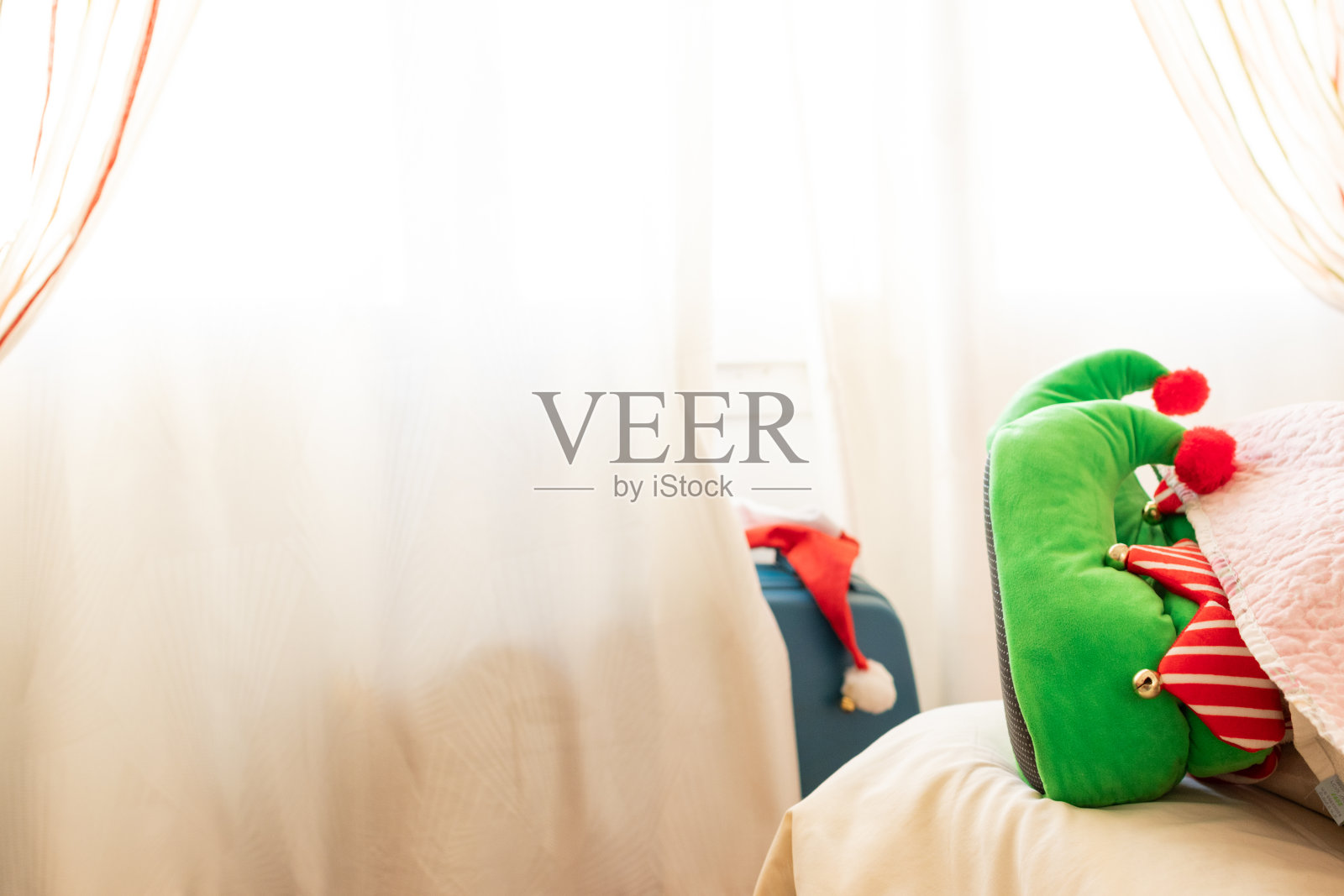 一个无法辨认的圣诞精灵躺在酒店房间的床上，旁边是他的行李箱和行李。照片摄影图片