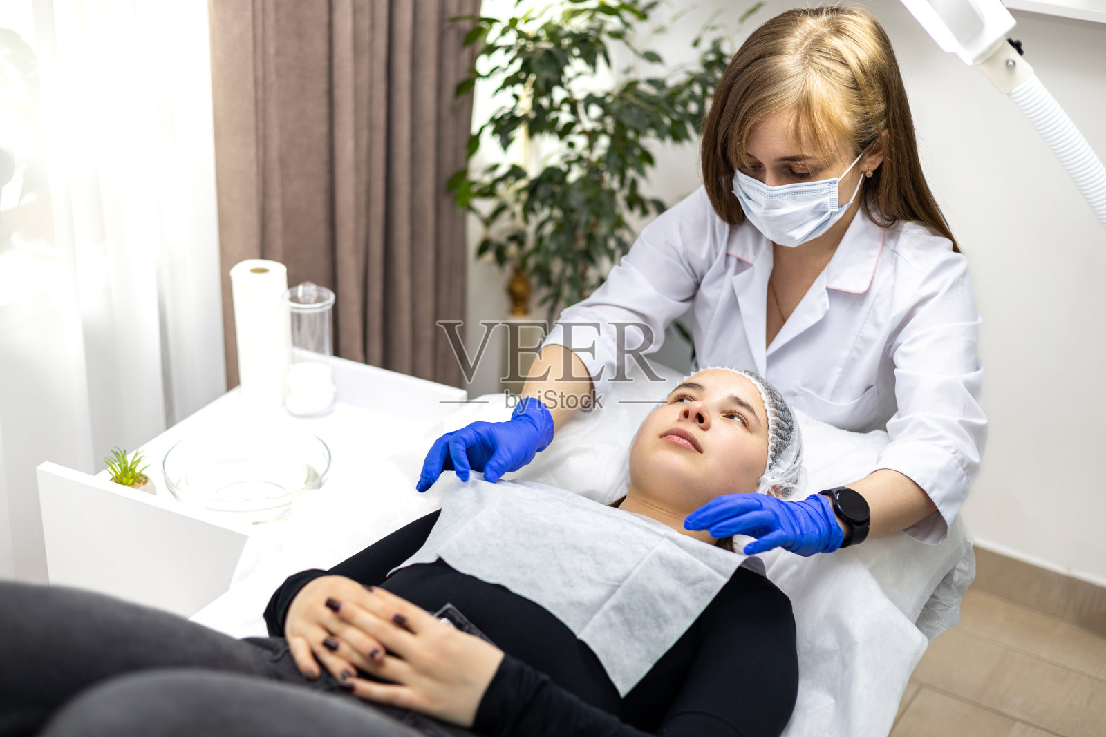 一位美容师为她的客户准备美容护理的画像。美容师戴着消毒手套和口罩。照片摄影图片