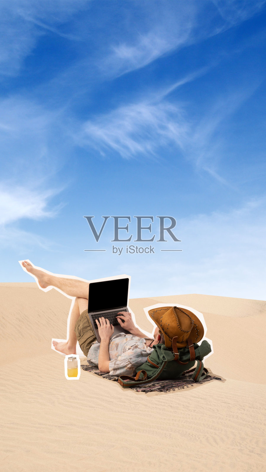 当代艺术拼贴。戴着帽子的男子斜倚在沙丘上，在笔记本电脑上打字，旁边放着饮料。适用于任何地方。抽象的艺术作品。照片摄影图片