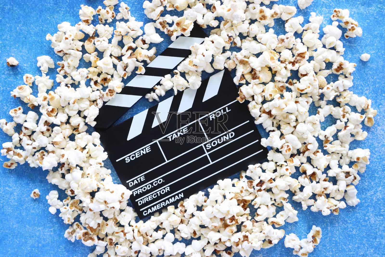 图片中黑色的隔板被洒出的爆玉米粒包围，打开的铰链隔板，斑驳的蓝色背景，抬高的视角照片摄影图片