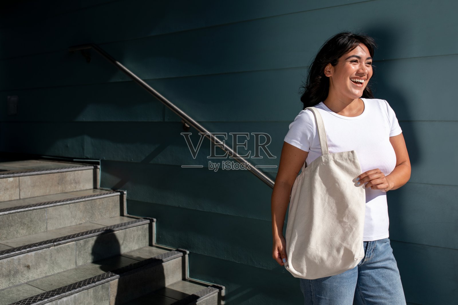 自信的拉丁女人，拿着一个普通的白色大手提袋，站在大学校园的楼梯上照片摄影图片