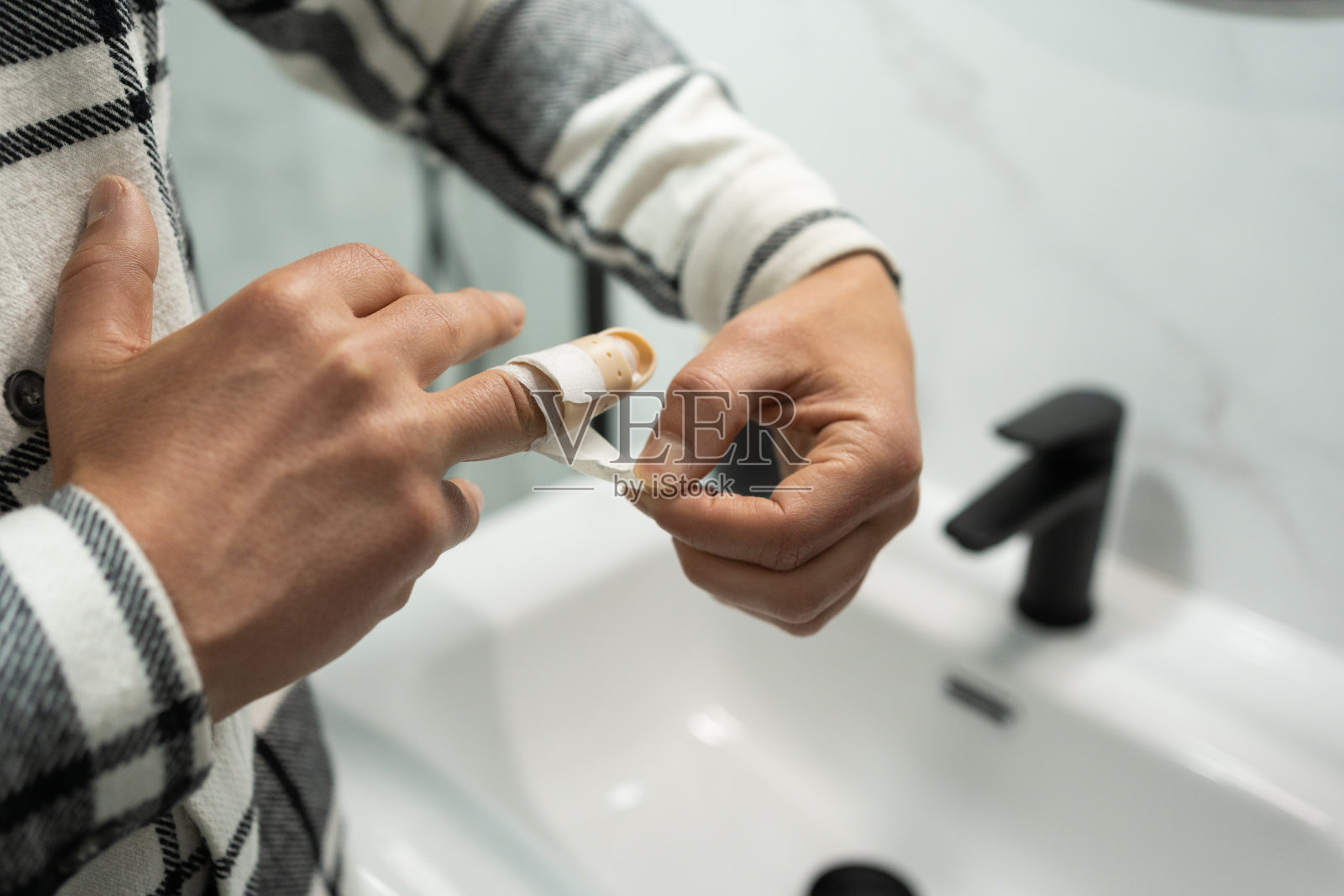 匿名年轻人用堆叠夹板从受伤手指上移除粘合剂。在浴室里，一个人小心地从受伤的手指上取下绷带。照片摄影图片