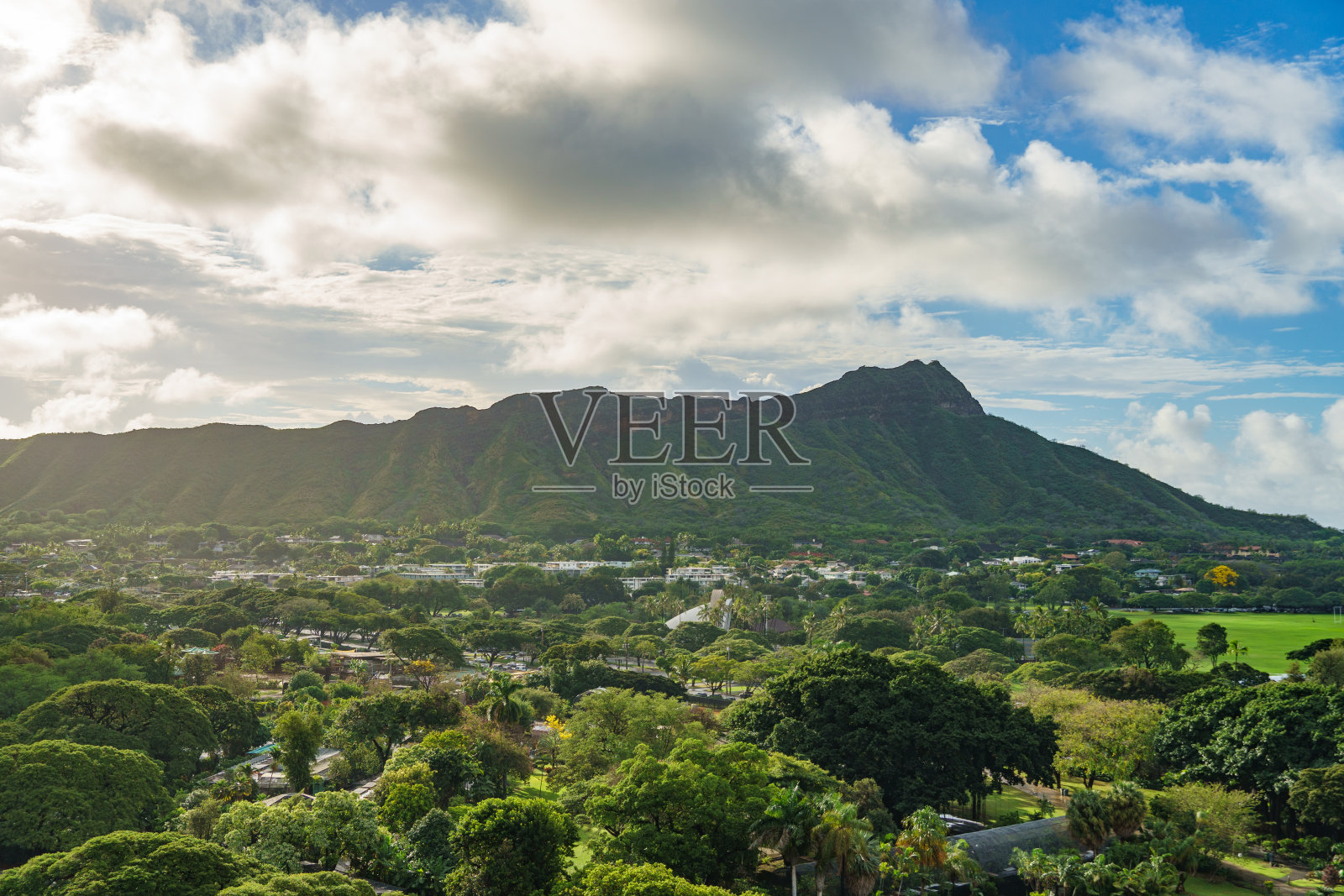 在多云的天空下，鸟瞰一座有树木、房屋、绿色植物的山照片摄影图片