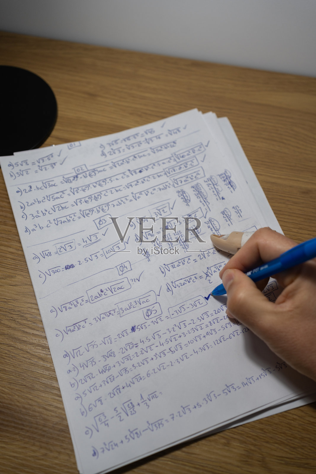 一个不认识的人的手在台灯下做平方根和分数的数学练习的特写。恢复与进步概念照片摄影图片