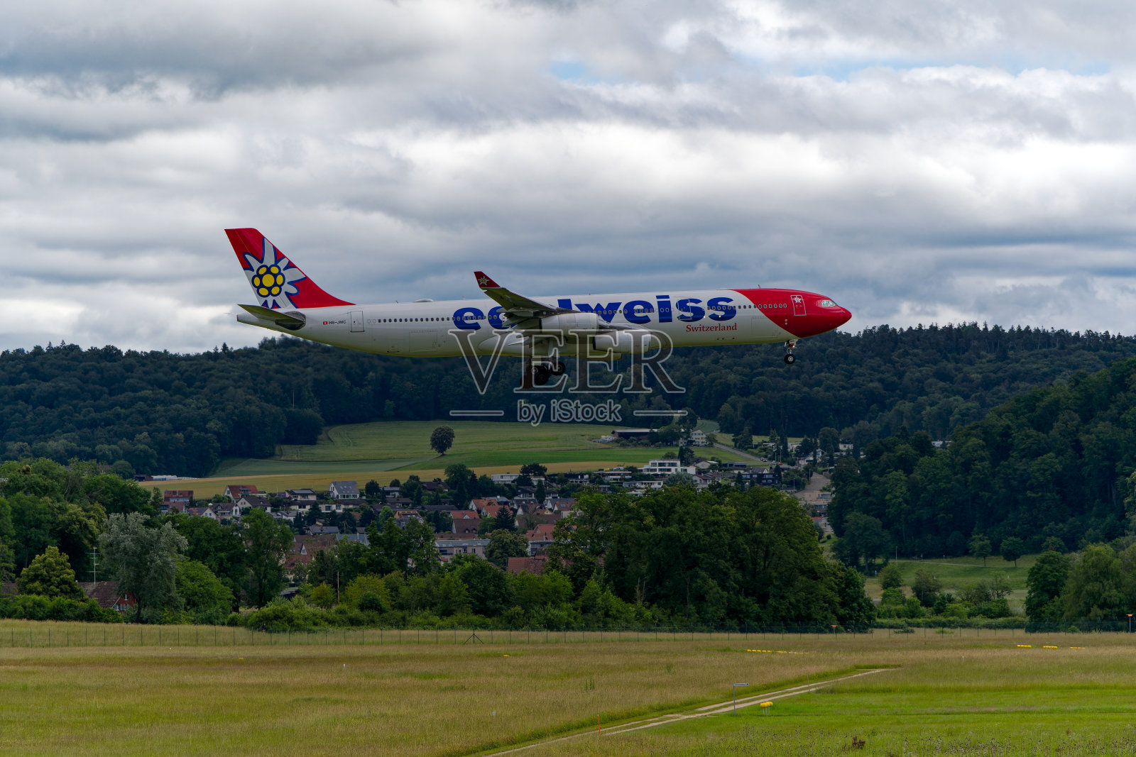 雪绒花航空公司的白、红、蓝三色瑞士飞机在瑞士机场最后进场时的侧视图。照片摄影图片