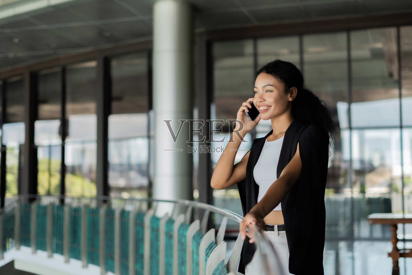 一位女士站在阳台上讲手机。她面带微笑，很享受她的谈话照片摄影图片