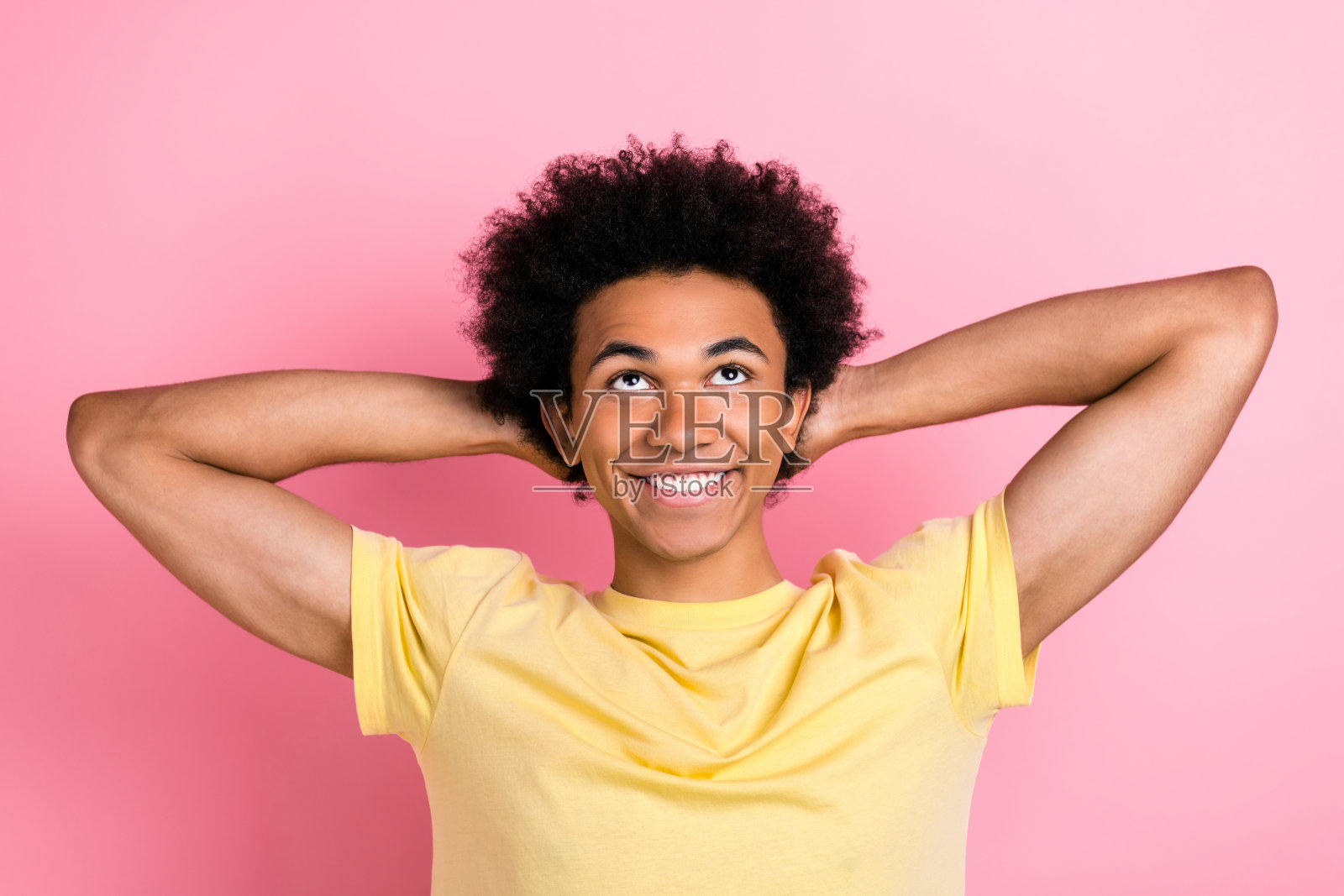 照片中开朗的人笑容满面，双手放在脑后，抬头看空，孤立在粉红色的背景上照片摄影图片