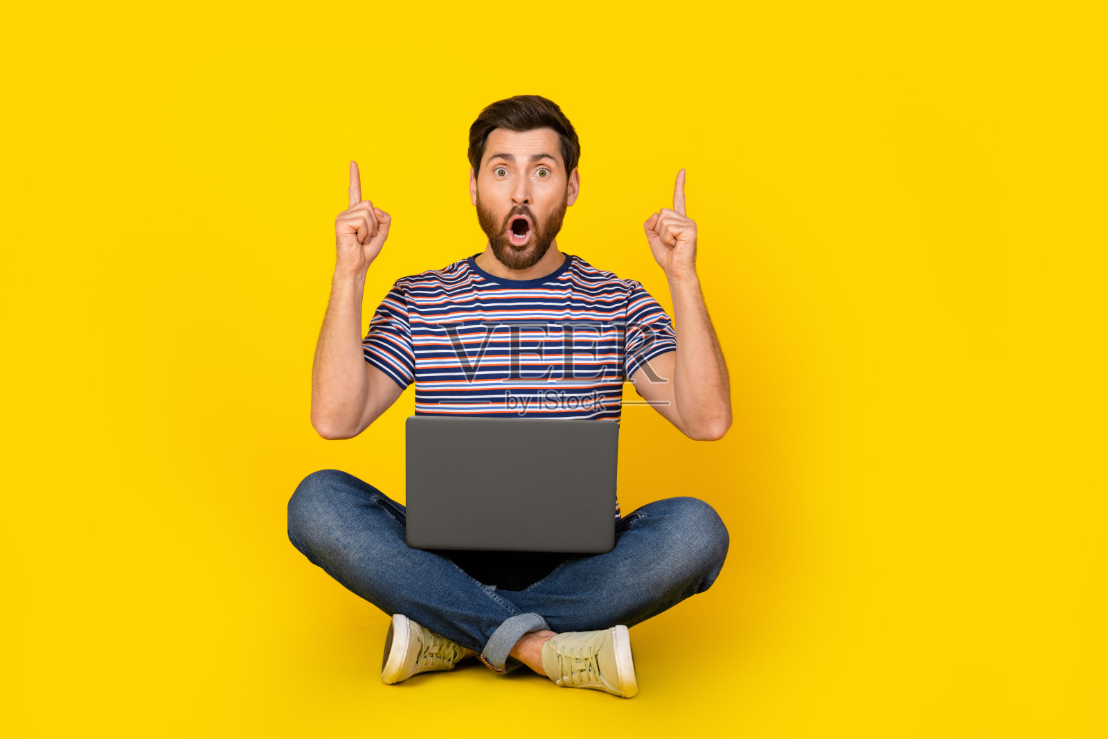 年轻的现代惊奇的家伙用笔记本电脑用小工具指导手指上面的copyspace孤立的黄色背景的照片照片摄影图片